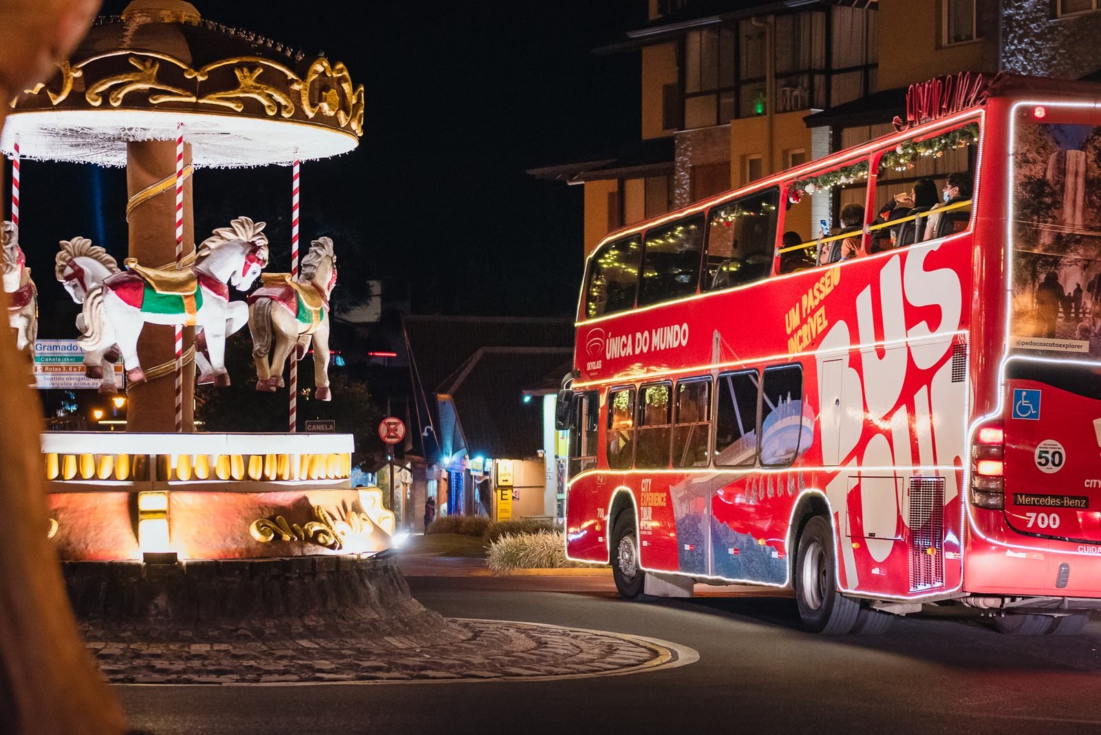 Ônibus vermelho iluminado passando ao lado de um carrossel decorado