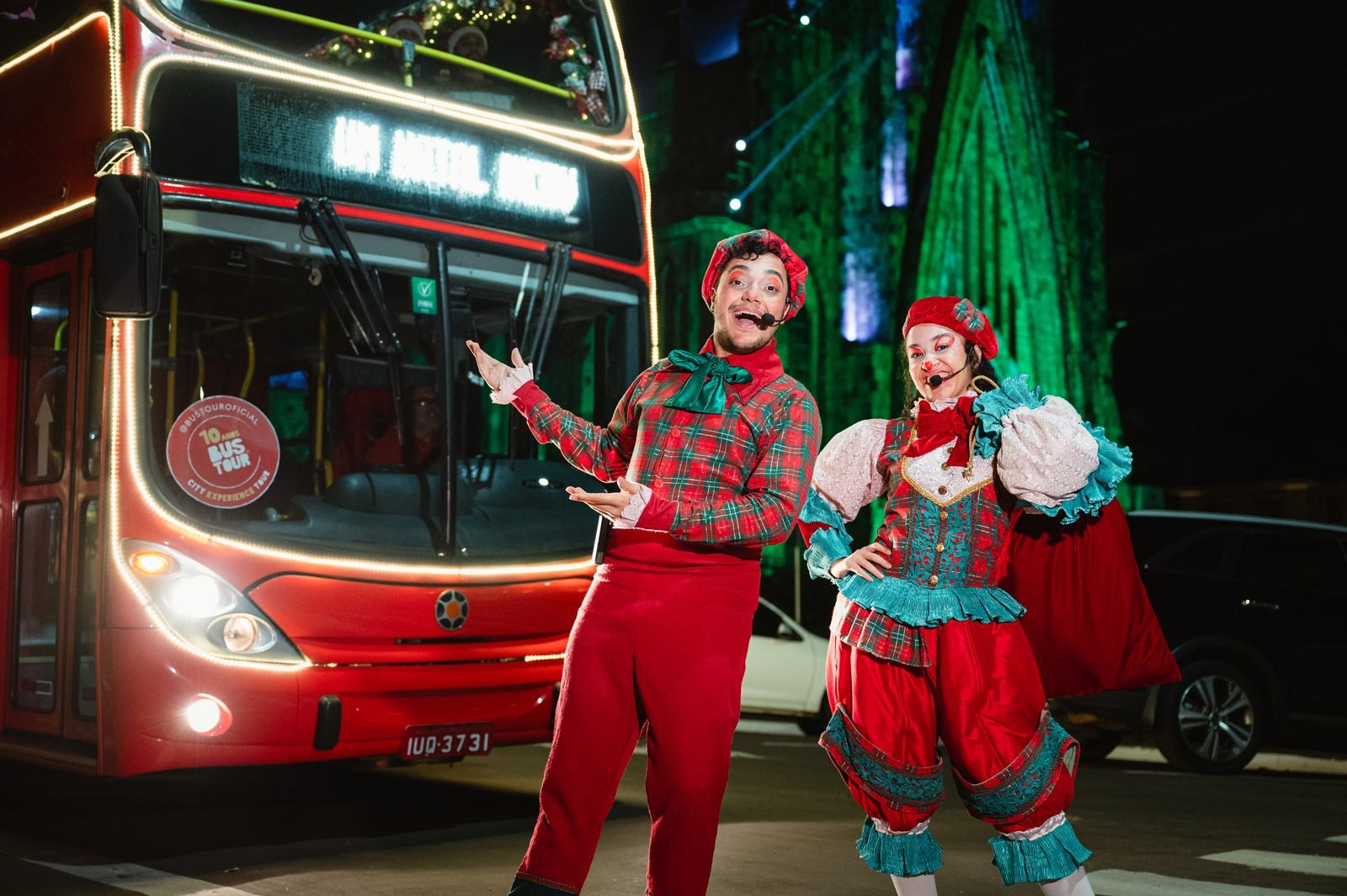 Dois artistas com microfone headset posando em frente ao ônibus iluminado