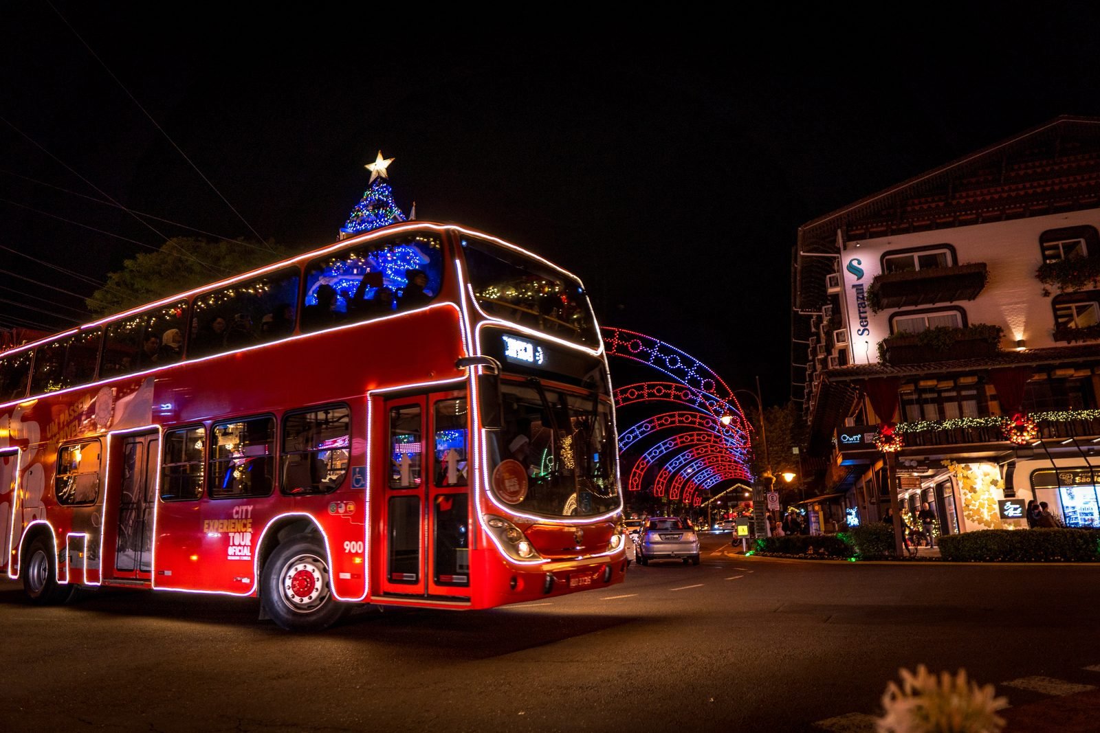 Ônibus iluminado ao lado de uma grande árvore de Natal decorada