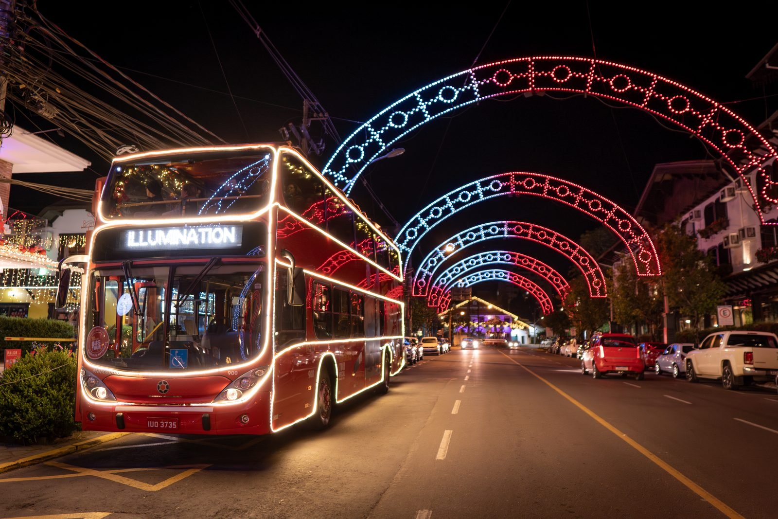 Ônibus de dois andares iluminado em avenida decorada com arcos de luzes