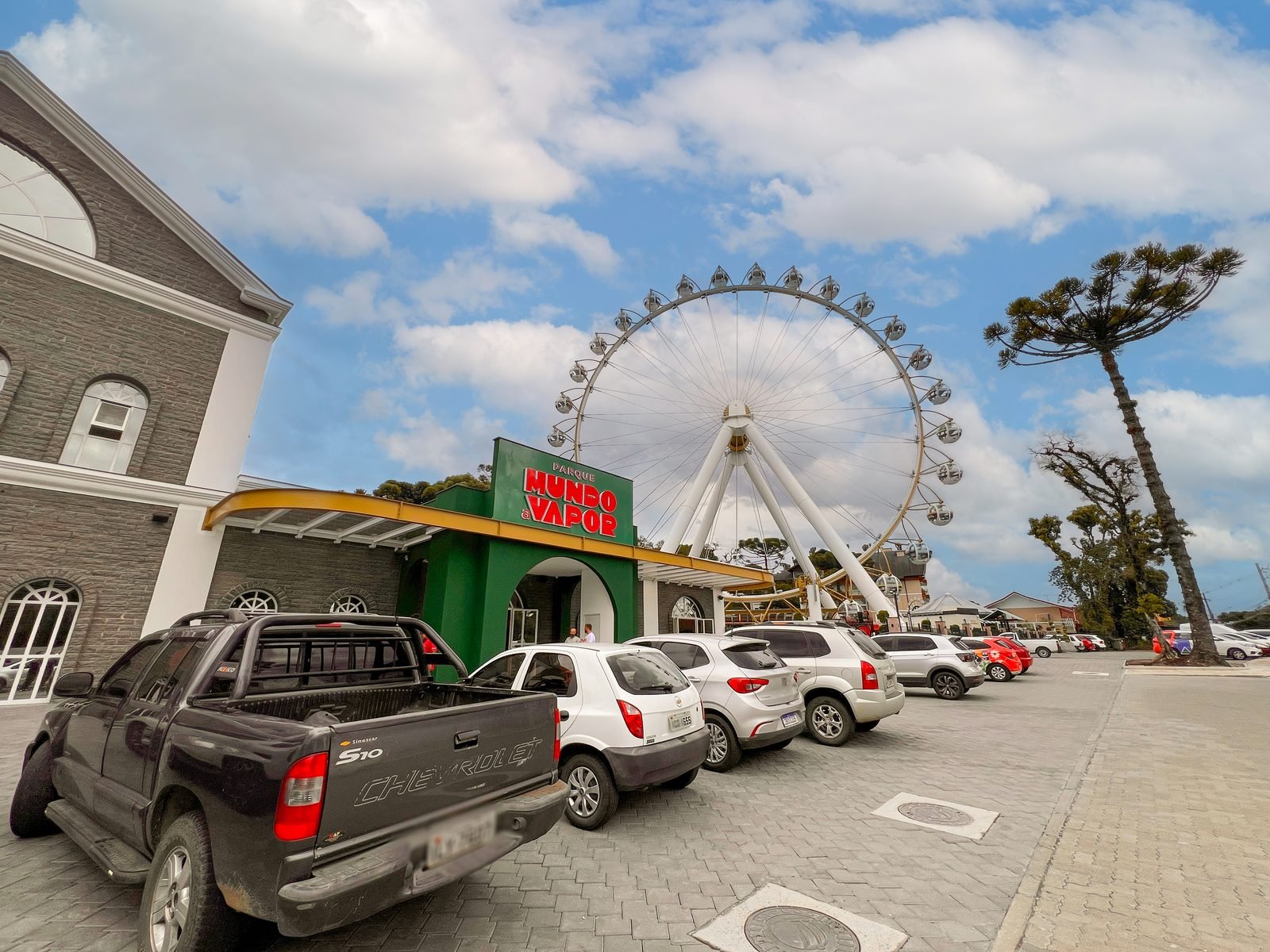 Entrada do Parque Mundo a Vapor com a roda gigante ao fundo e araucária à direita